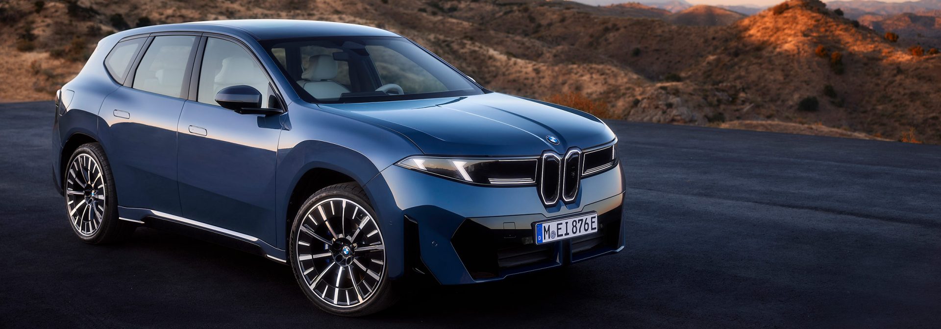 The new BMW iX3 in blue on an empty road with sand dunes in the background.