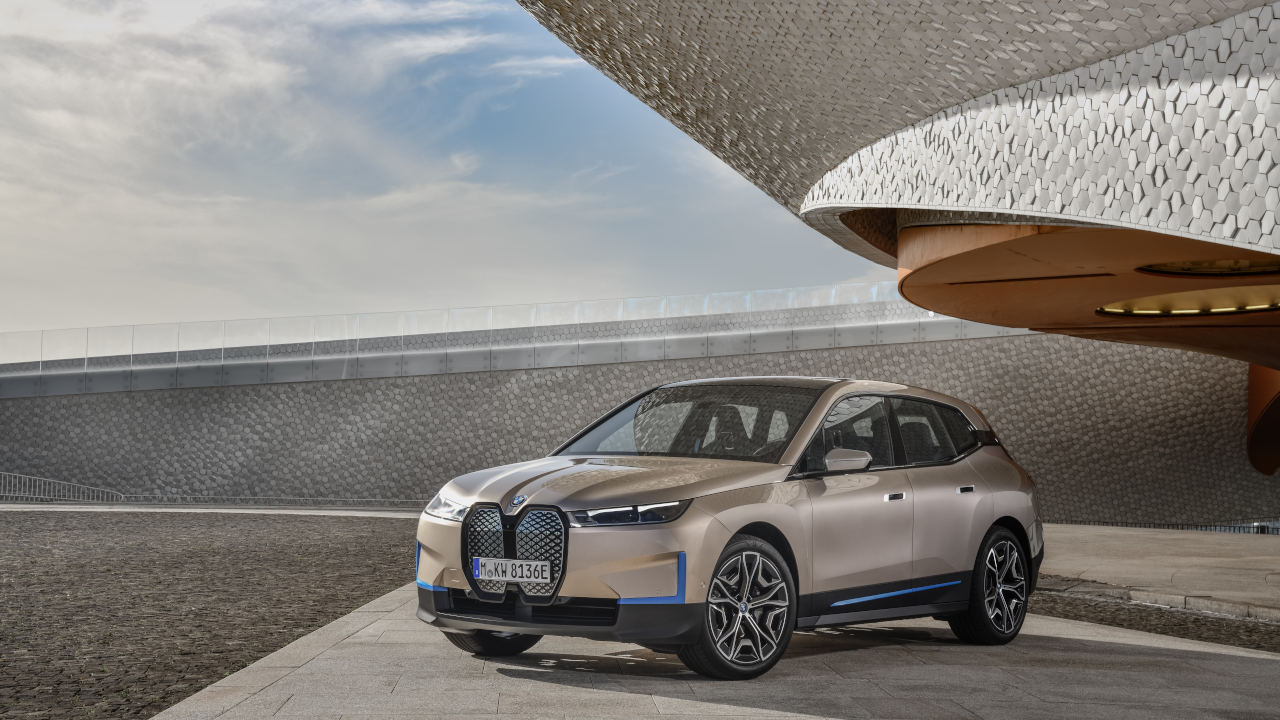 A BMW electric SUV parked on a concrete surface in front of modern architecture with a curved, textured roof design.