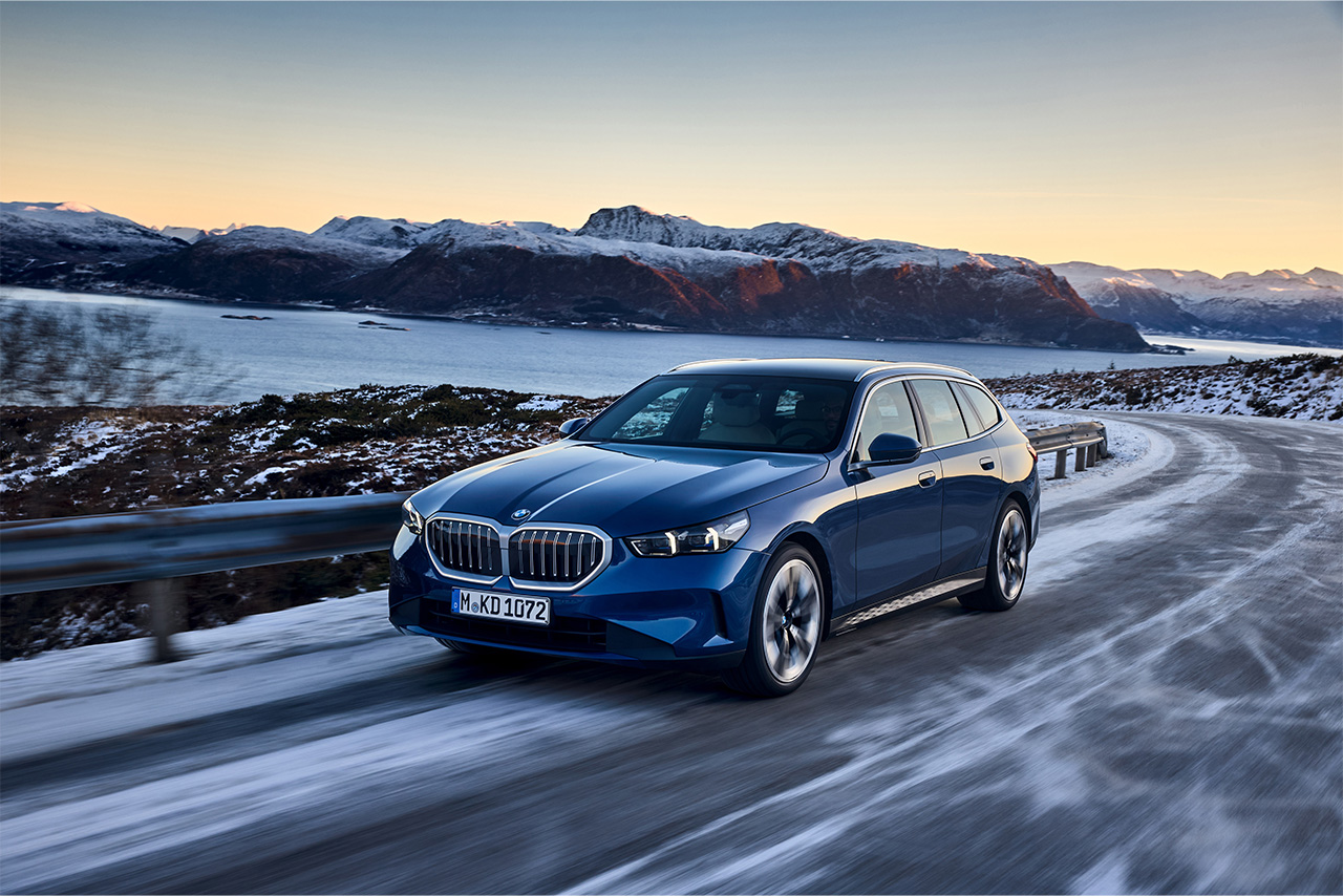 A blue BMW 5 Series Touring on the road in a snowy mountain landscape.