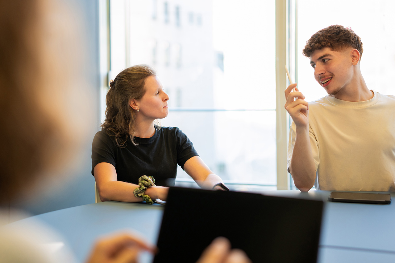 Two persons sit at a table and use a laptop for their work.