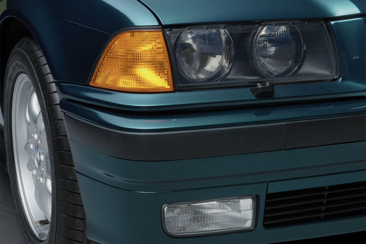 A glass panel covers the double headlight: Detail view of the front right headlight in a green BMW E36 Coupe.