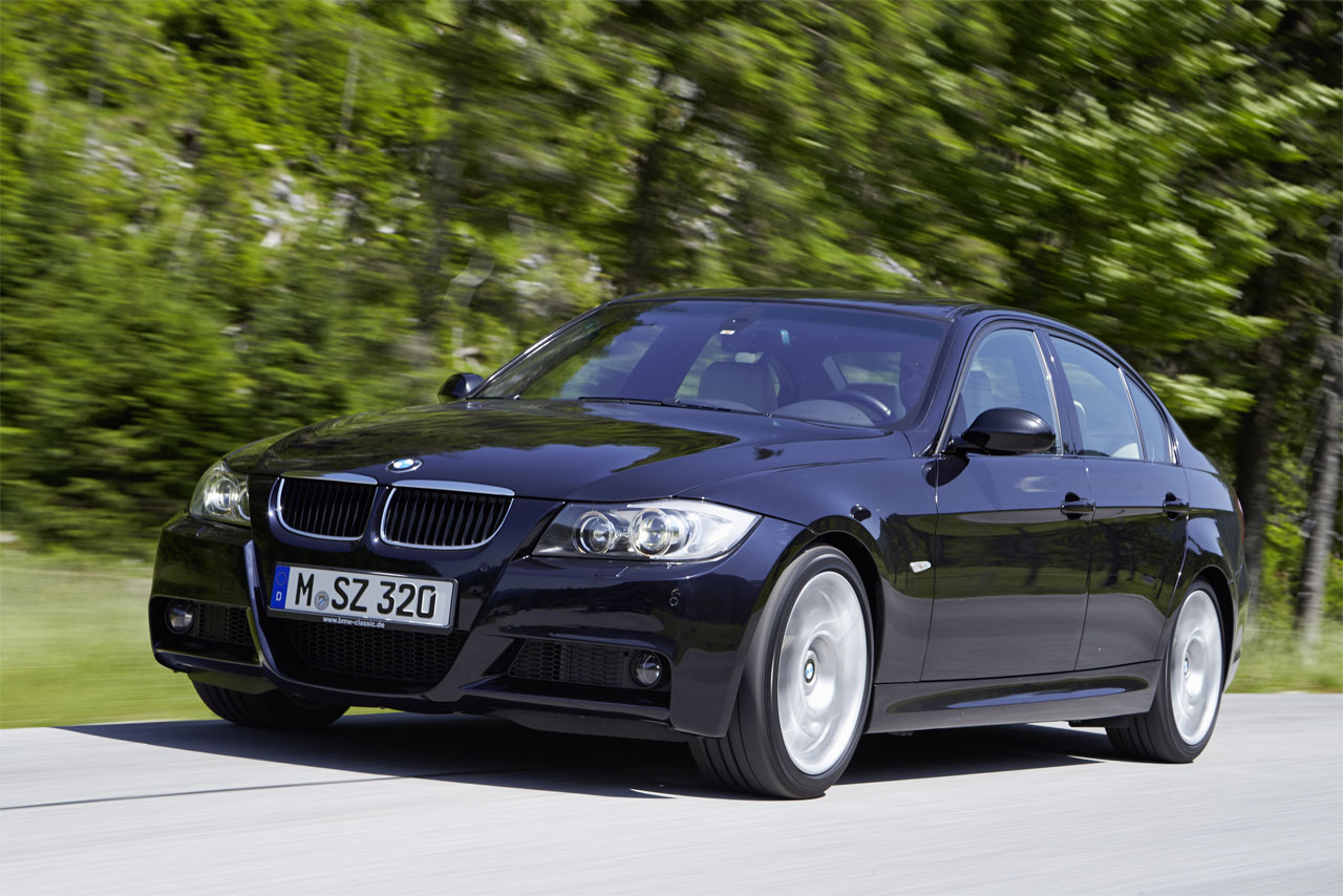 A BMW E90 Sedan seen from the front left as it drives dynamically along a country road