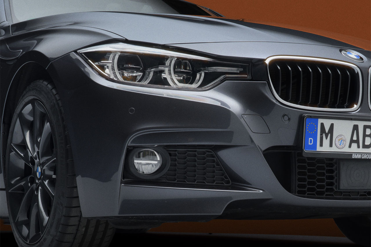 A closeup of the right-hand headlight unit and fog light of a black BMW F30 Sedan.