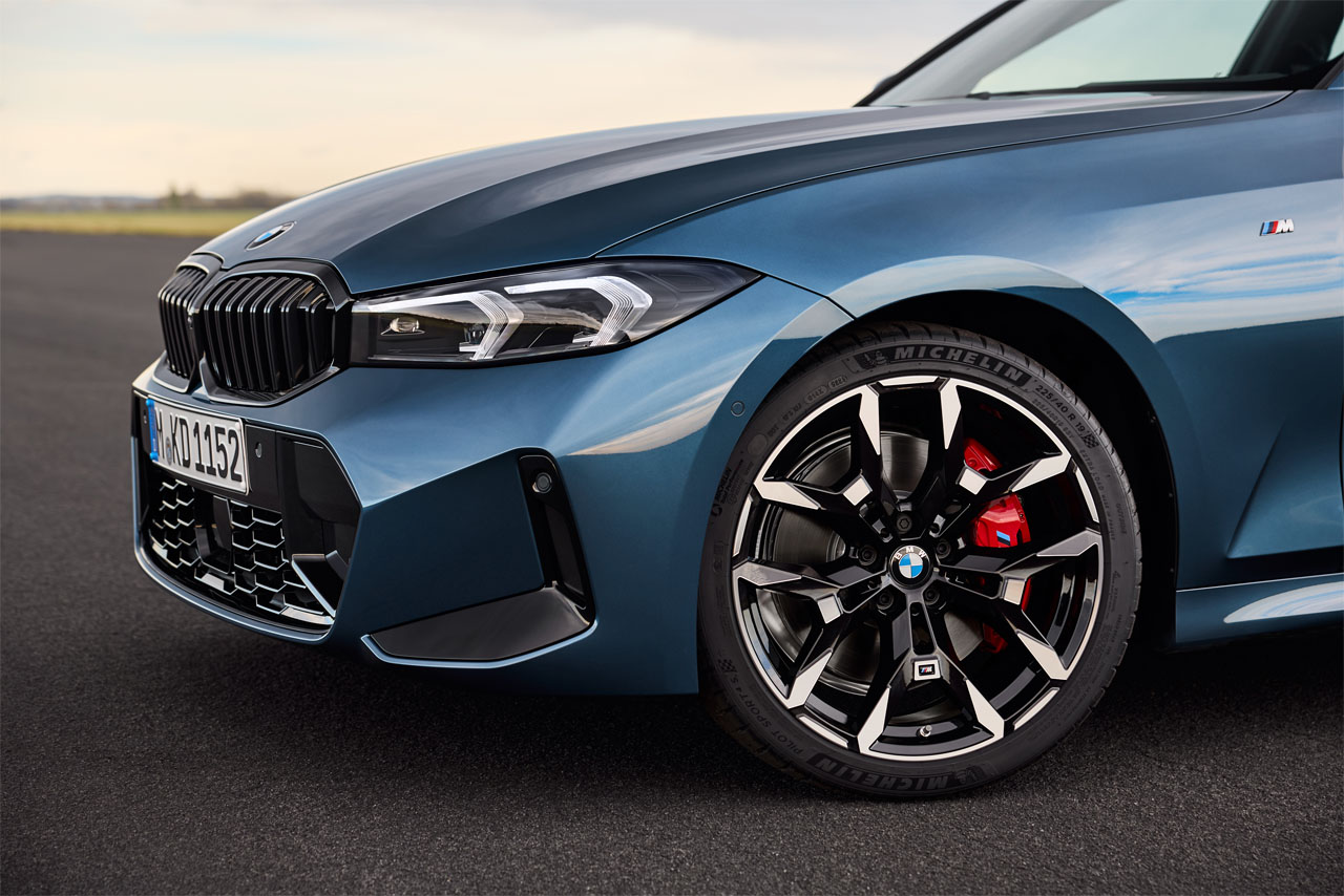 Detail shot of the front of a blue BMW 330i (G20), viewed from the left to show the headlights and sporty, elegant light alloy wheels.