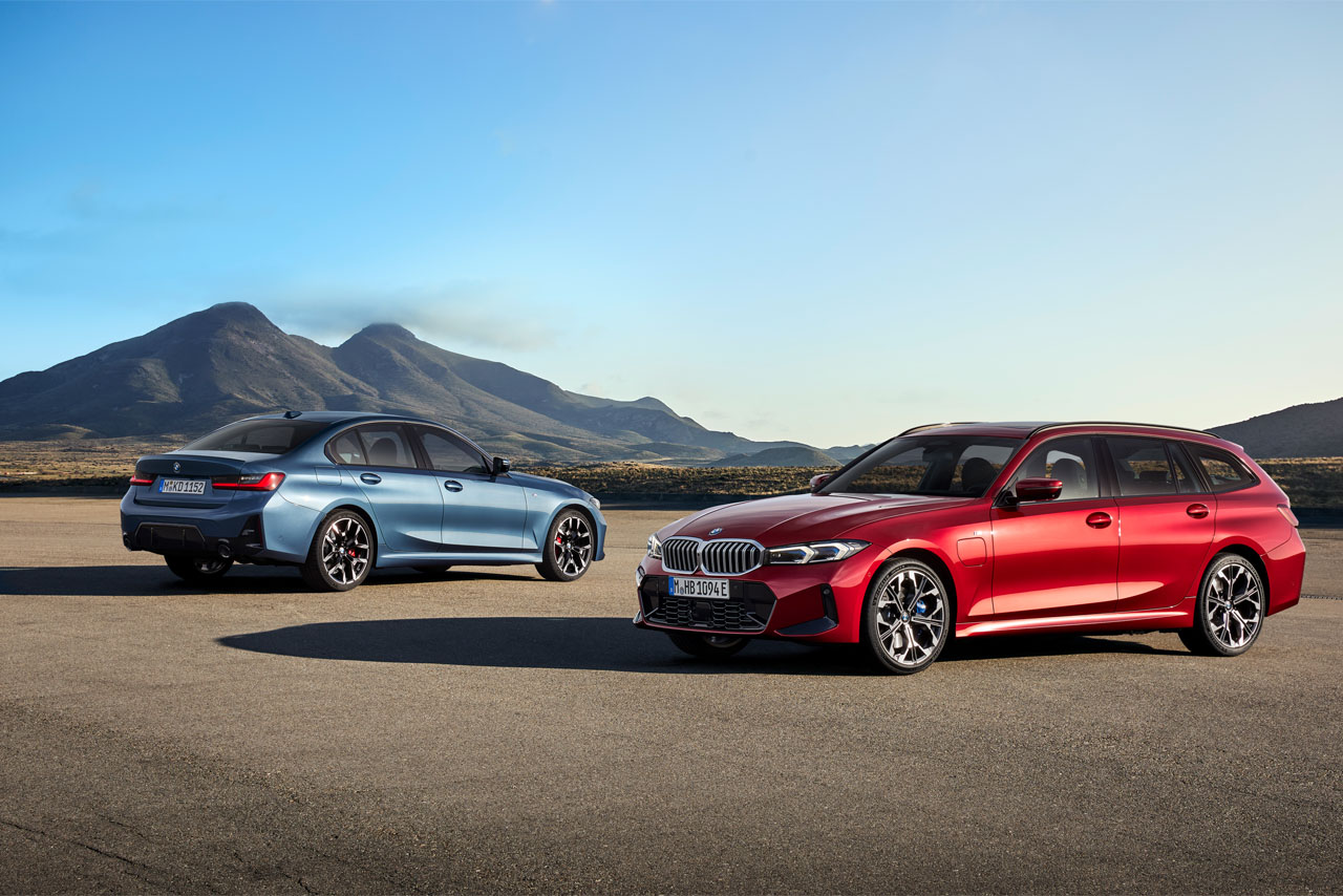 A red BMW 330e Touring (G20) in the foreground with a blue BMW 330i Sedan (G20) behind it and mountains in the background.