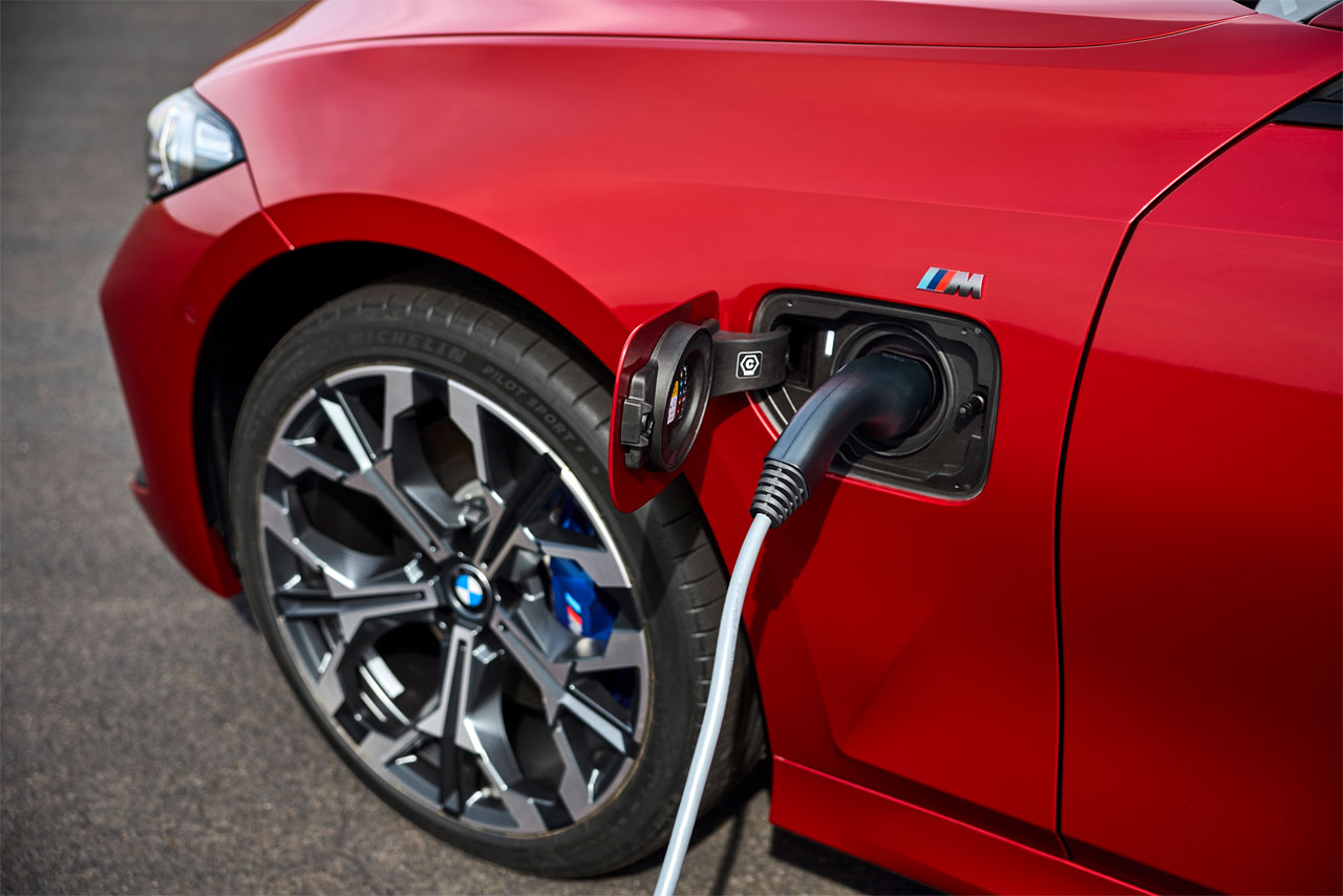 Closeup of the charging cable in the connector in the front left wing of a red BMW 330e Touring (G20).