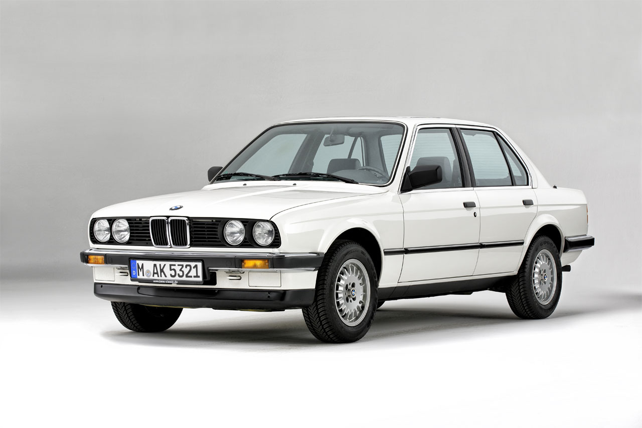 A four-door BMW E30 Sedan in white, seen from the front left.