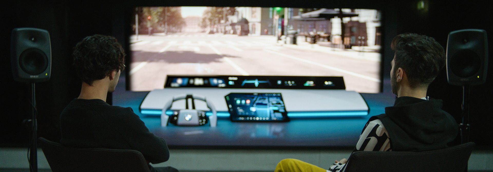 Two BMW Group sound designers in their studio, surrounded by tech, look at a virtual front screen with BMW Panoramic iDrive.