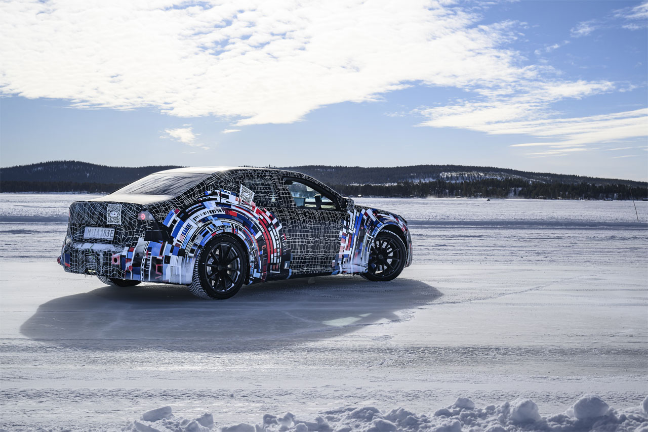 Side view of a BMW M prototype from the latest generation in striking camouflage on a frozen lake in a Nordic landscape during cold-weather testing.