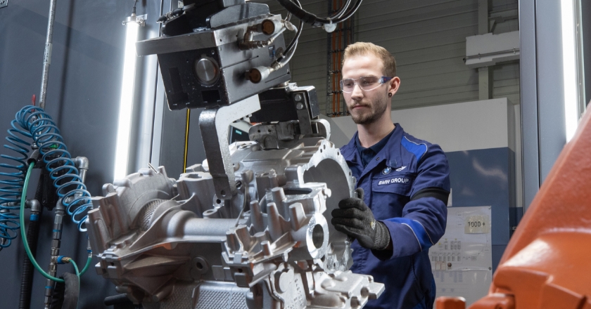 A person in protective clothing and goggles stands behind a technical tool and operates it.