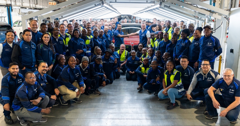 Many people are scattered around a red BMW car in a factory hall.