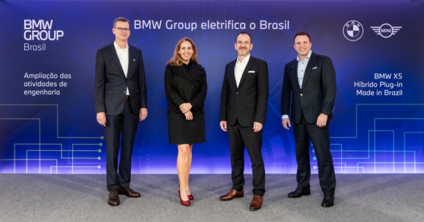 Four people stand in front of a blue screen with the logos of the BMW and MINI brands and the words “BMW X5 Hibrido Plug-in Made in Brasil”.