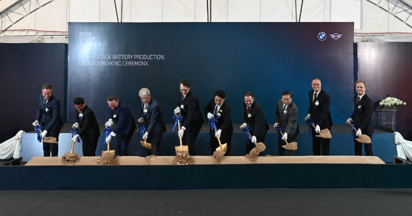 Ten people stand in front of a dark screen for a ground-breaking ceremony.