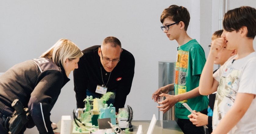 A policewoman, a man and three children are standing at a table with colourful craft materials.