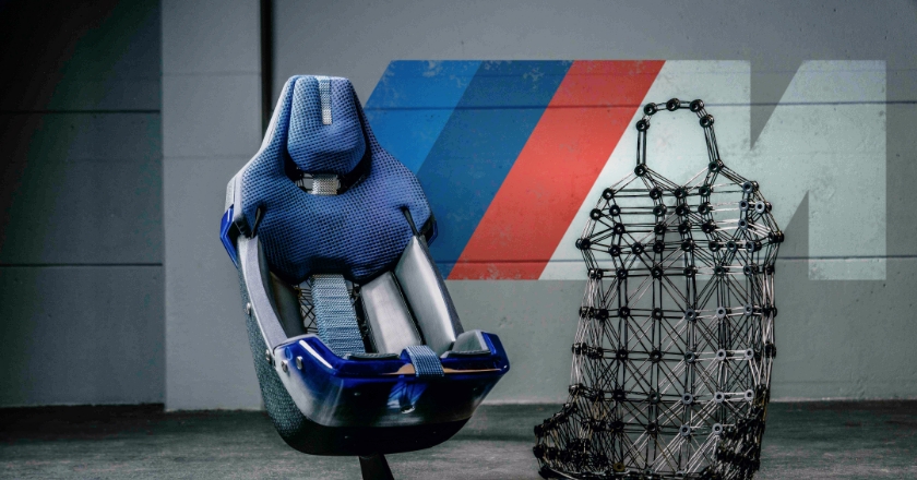 In front of a wall with the BMW M logo is a car seat on the left and the matching frame of the car seat on the right.