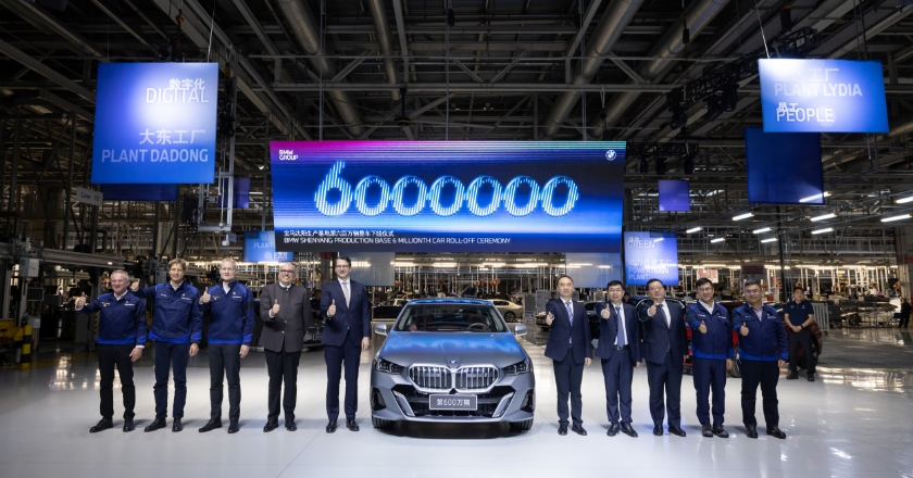 In a factory hall, ten men surround a car and give it the thumbs up.
