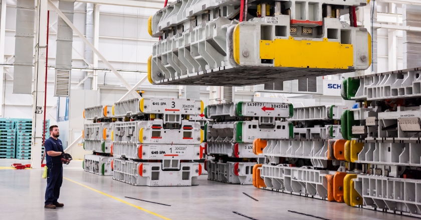 A man stands in a factory hall and controls a large workpiece by remote control.