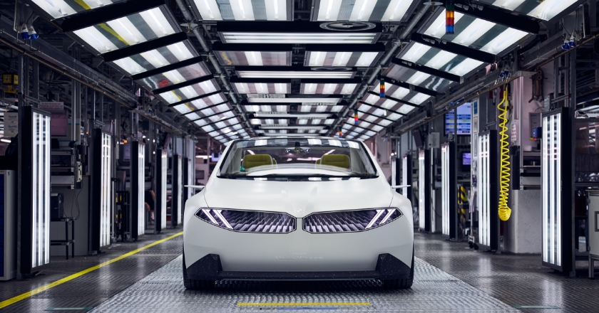 The BMW Vision NEUE KLASSE vision vehicle stands frontally in a production plant with many lights.