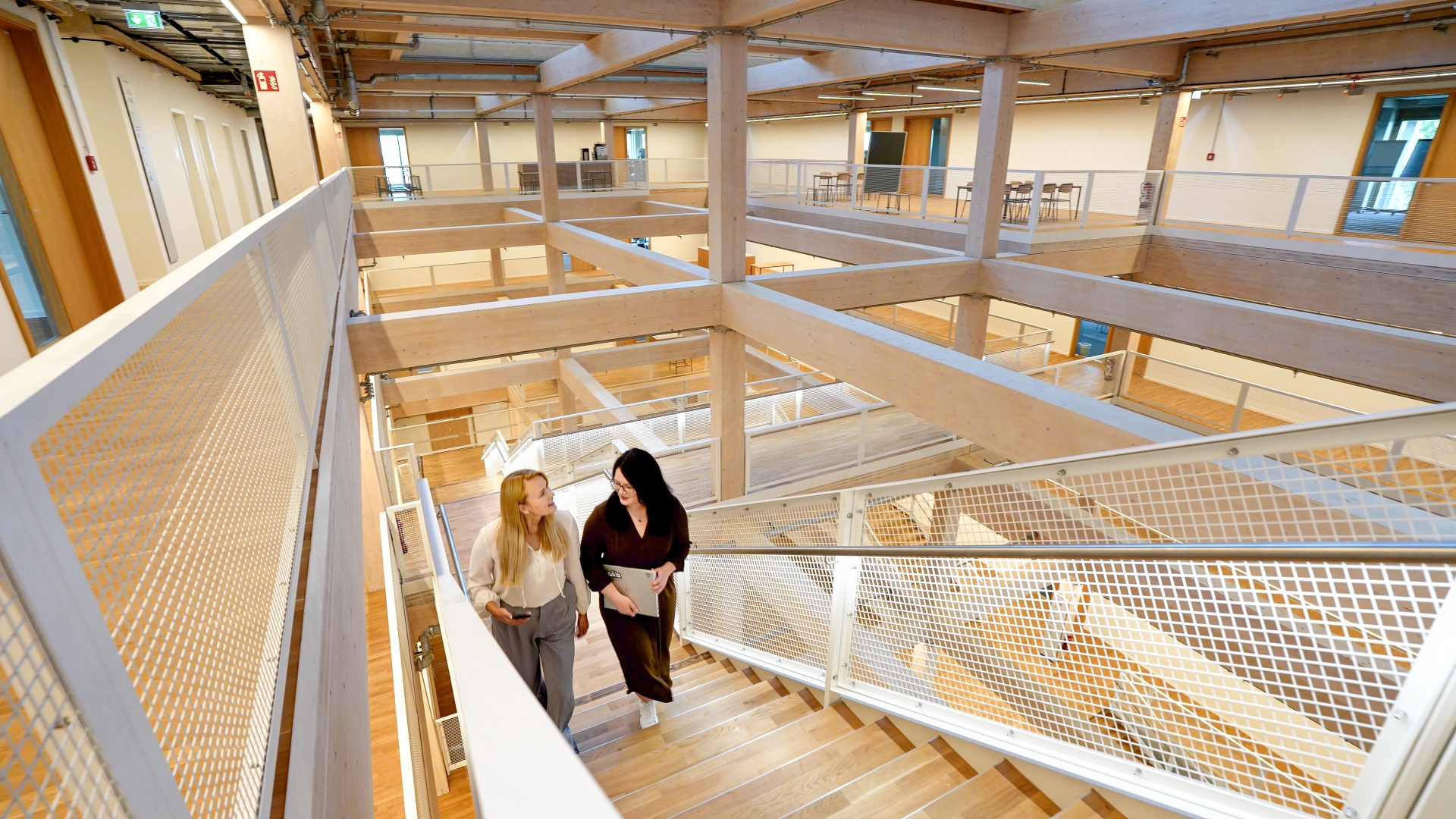 Interior space with open wooden structures and staircase where two people walk upward.