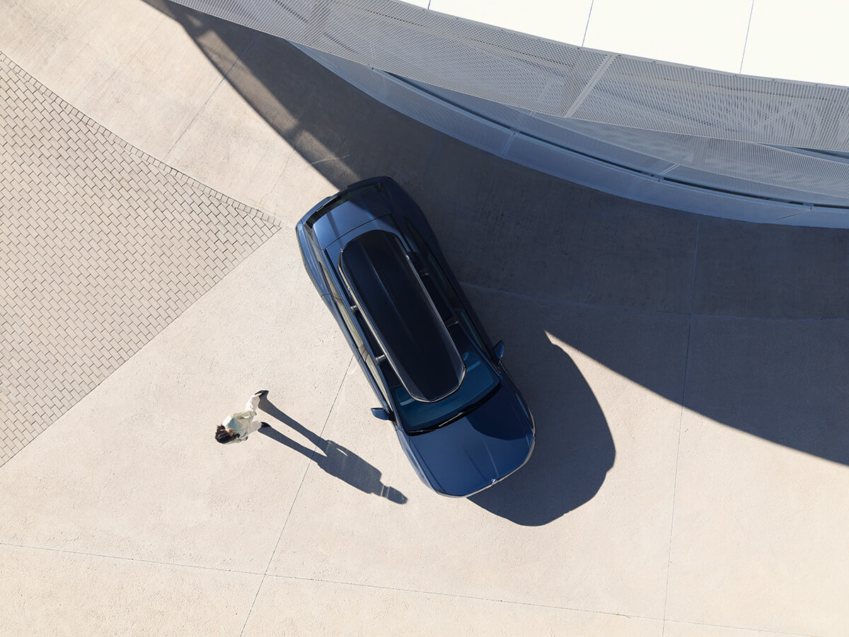 Top-down view of a BMW vehicle next to a single person on a bright paved area.