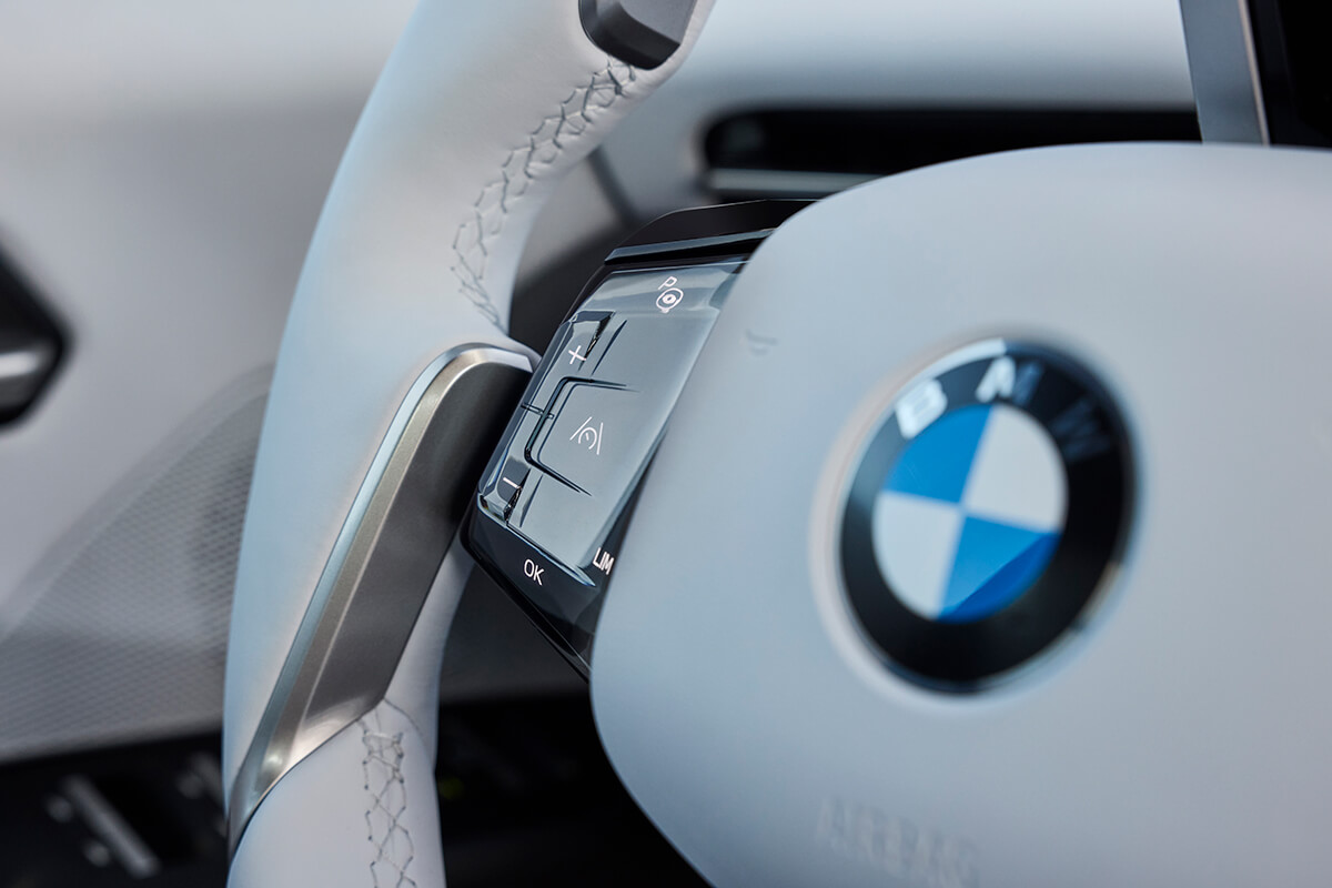 BMW steering wheel with integrated control buttons in the foreground of a bright interior.