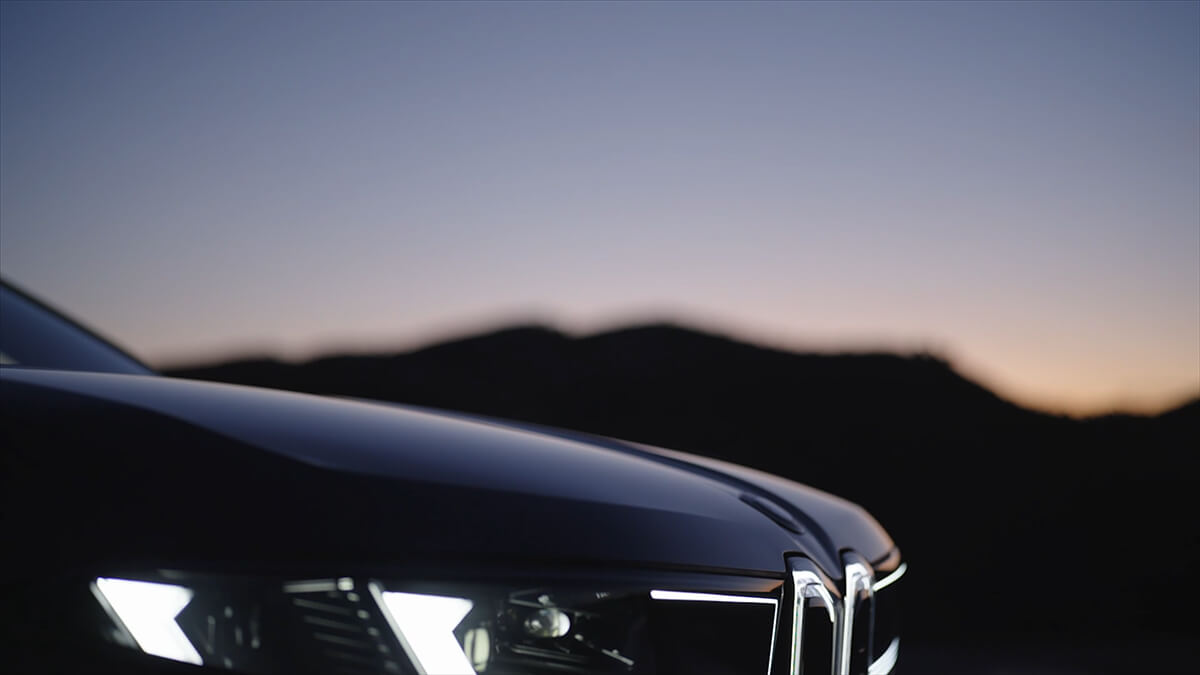 Front section of a BMW vehicle with illuminated LED headlights in front of mountain silhouettes at dusk.