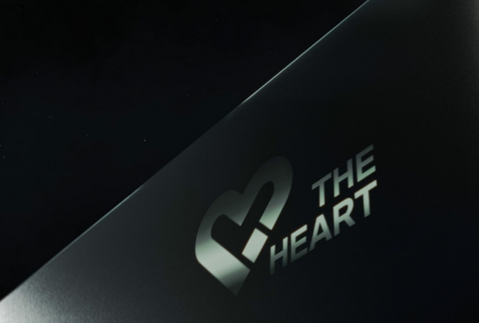 A battery cell is held by a hand in a glove above a white table, there a blurred upper body dressed in white in the background.