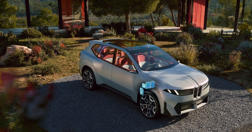 BMW concept vehicle on a circular outdoor area in front of modern architecture, accompanied by graphic elements indicating vehicle technology.