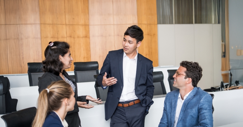 Discussion among a small group in a modern conference room, with a conversational setting around a table in a business environment.