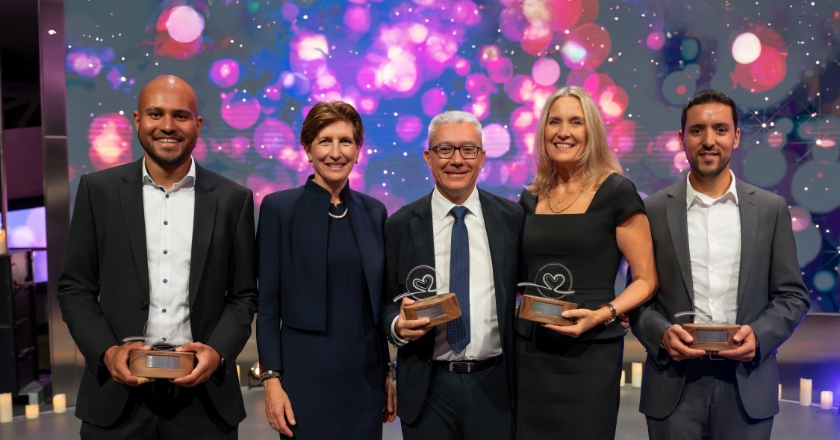Five people stand before an illuminated backdrop, four holding awards, surrounded by decorative LED candles.