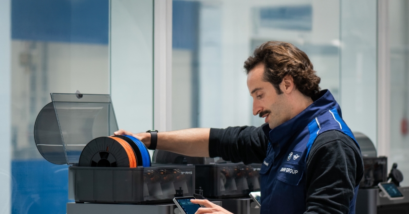 Person at a 3D‑printing station loads filament spools and operates the display of a Bambu Lab device.