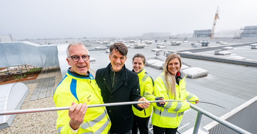 Four people in safety gear stand on an industrial rooftop holding a long cable together.