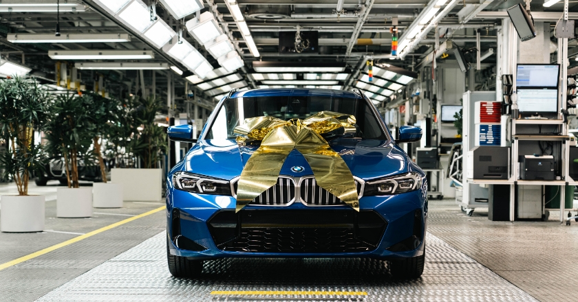 Blue BMW vehicle in the production hall with a large golden ribbon on the bonnet.