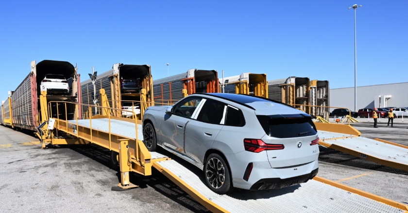 Grey BMW vehicle drives up a ramp into a car transport wagon, with additional vehicles already positioned inside.