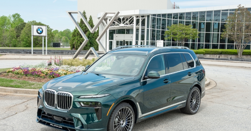 Dark green BMW SUV with Alpina details positioned in front of the plant entrance with modern glass façade and X sculpture.