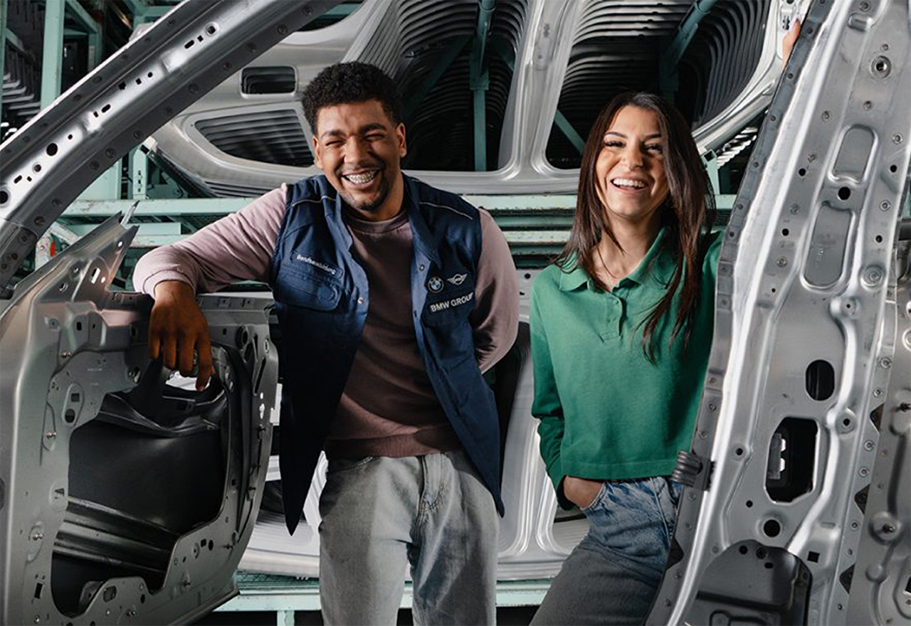 Two young BMW employees smile at the camera through a car body.