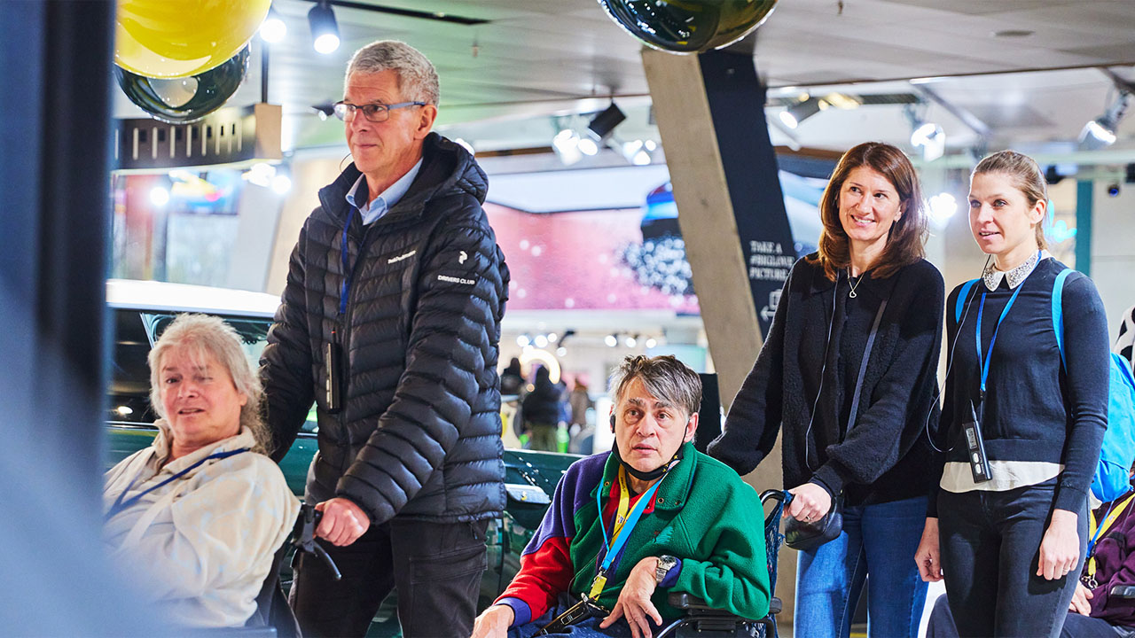 A group of people are smiling in front of a large photo depicting them.