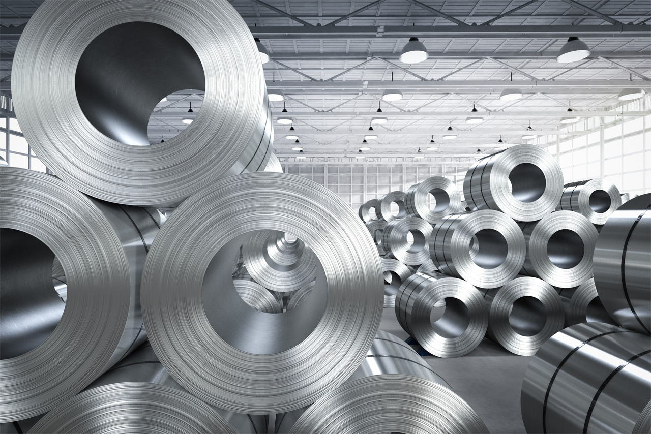 Large steel rolls are stacked on top of each other in a warehouse.