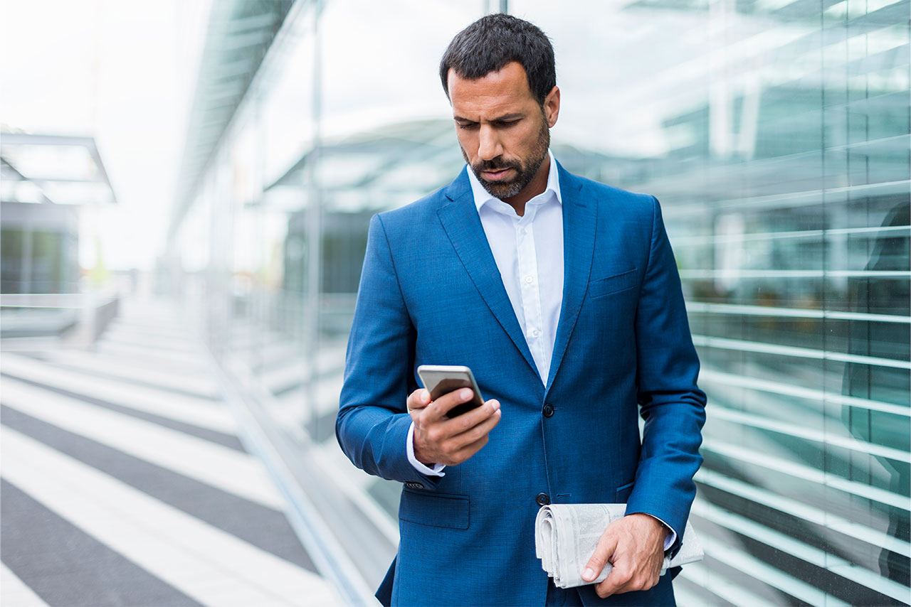 A man wearing a blue suit looks at his cell phone.