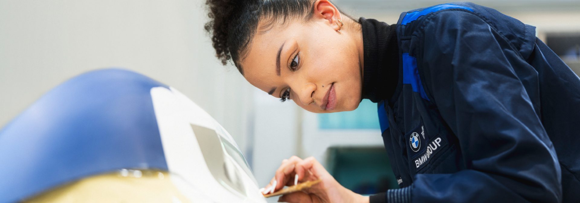A woman in a blue jacket is working on painting a car.
