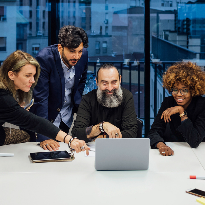 Five people standing together around a computer and talk about something.