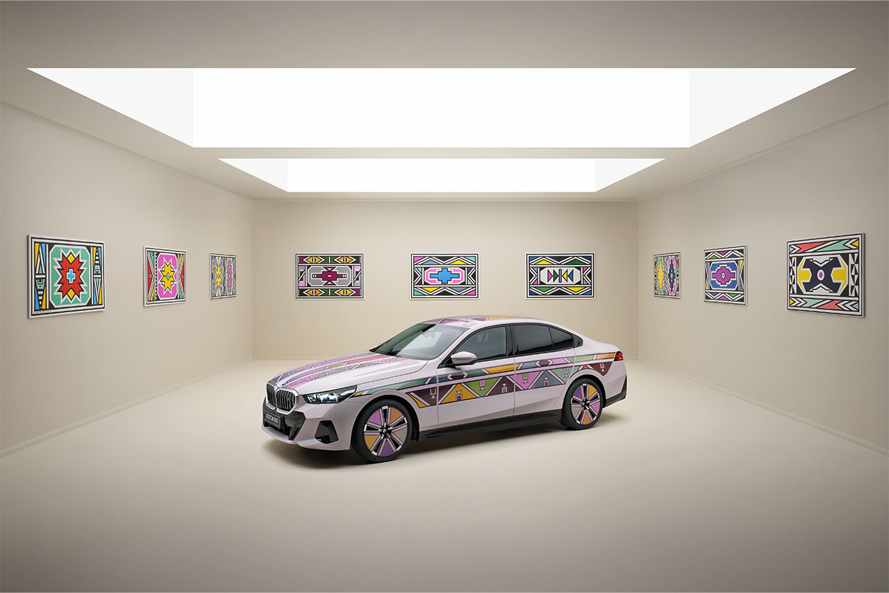 A white BMW 5 series with colorful patterns on it, the same patterns can be found as pictures on the wall.
