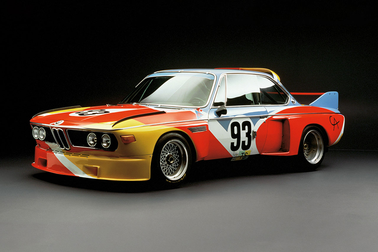 A classic BMW 3.0 CSL race car with a vibrant paint job featuring red, yellow, and blue colors.