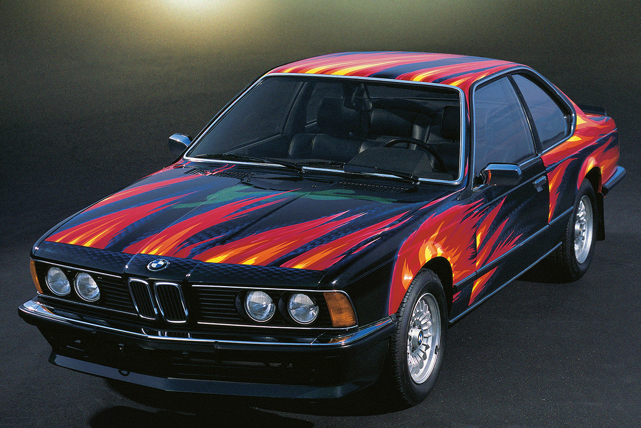 A BMW 635 CSi featuring a vibrant custom paint job with flames in red, orange, and yellow.